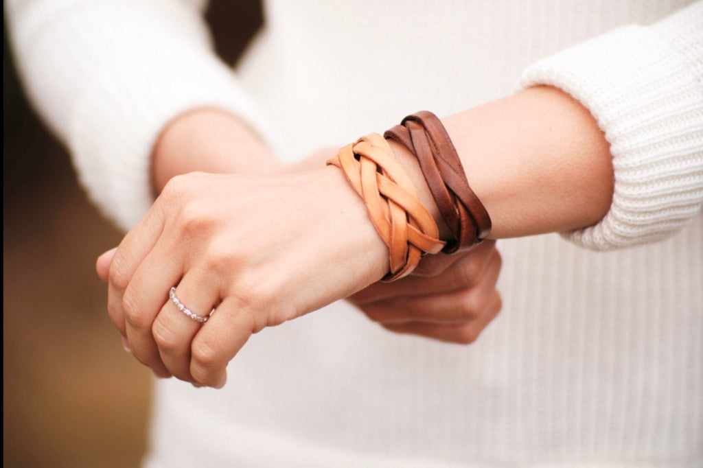 Two hands holding each other, wearing braided leather bracelets.