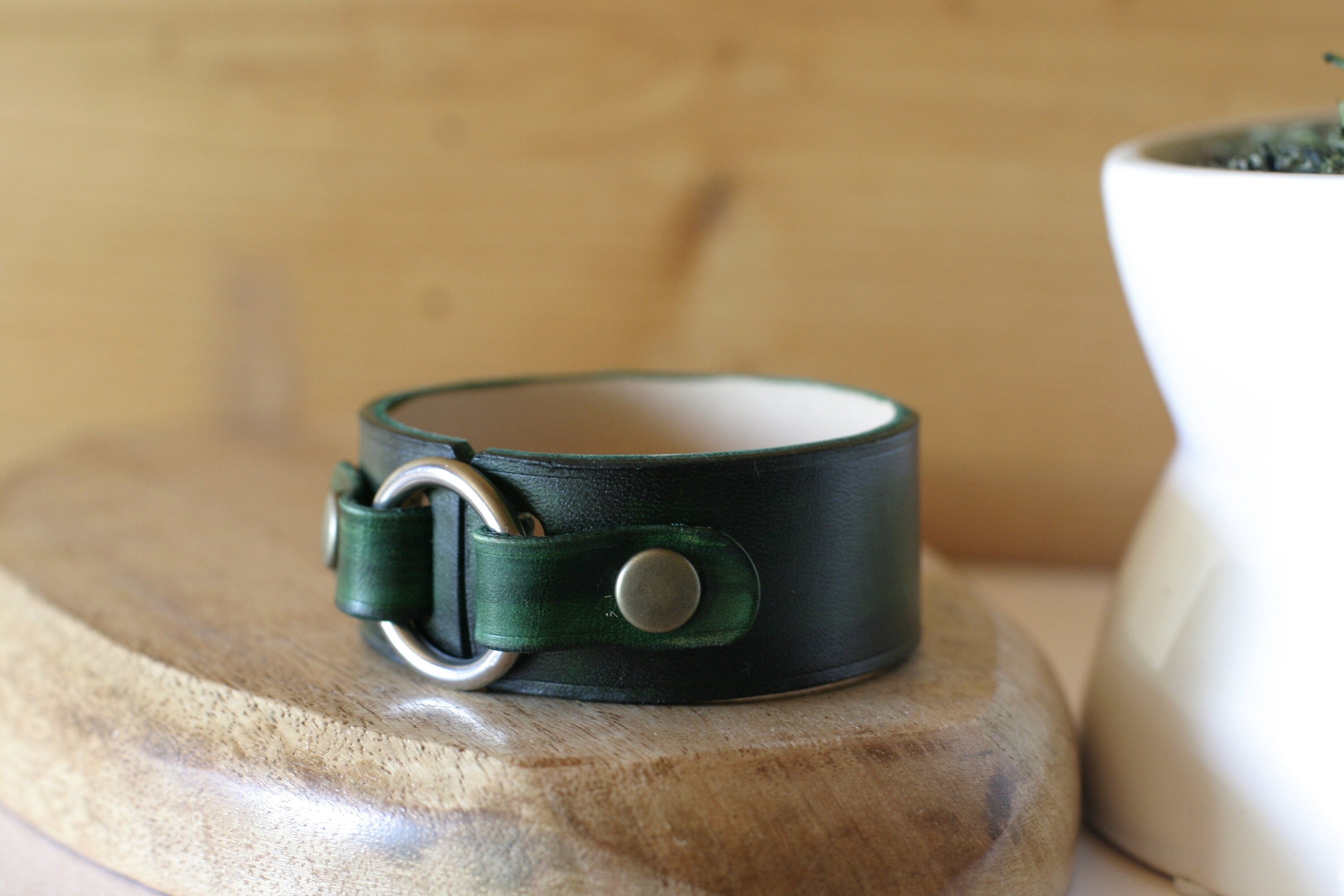 Green leather bracelet with silver buckle on a wooden surface