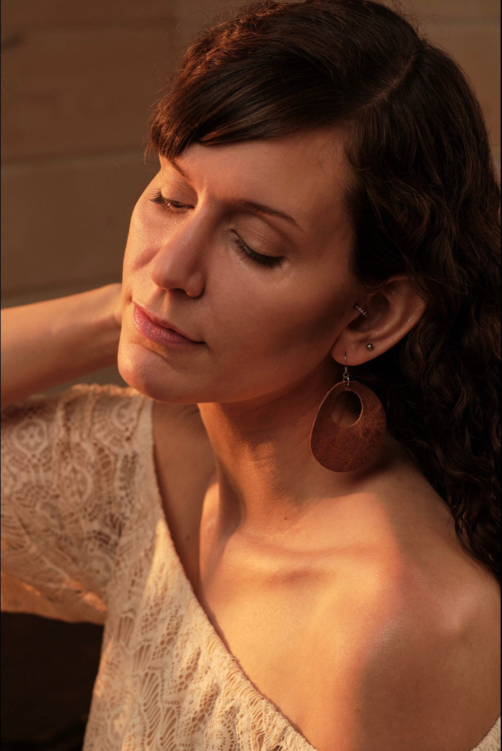 Woman wearing large wooden hoop earrings with a warm-toned background