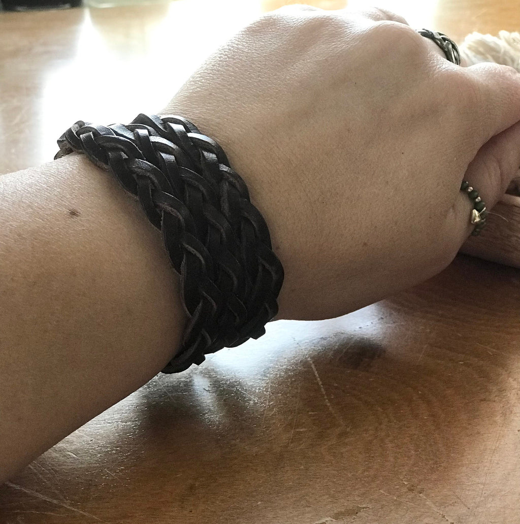 Black braided bracelet on a wrist against a wooden surface