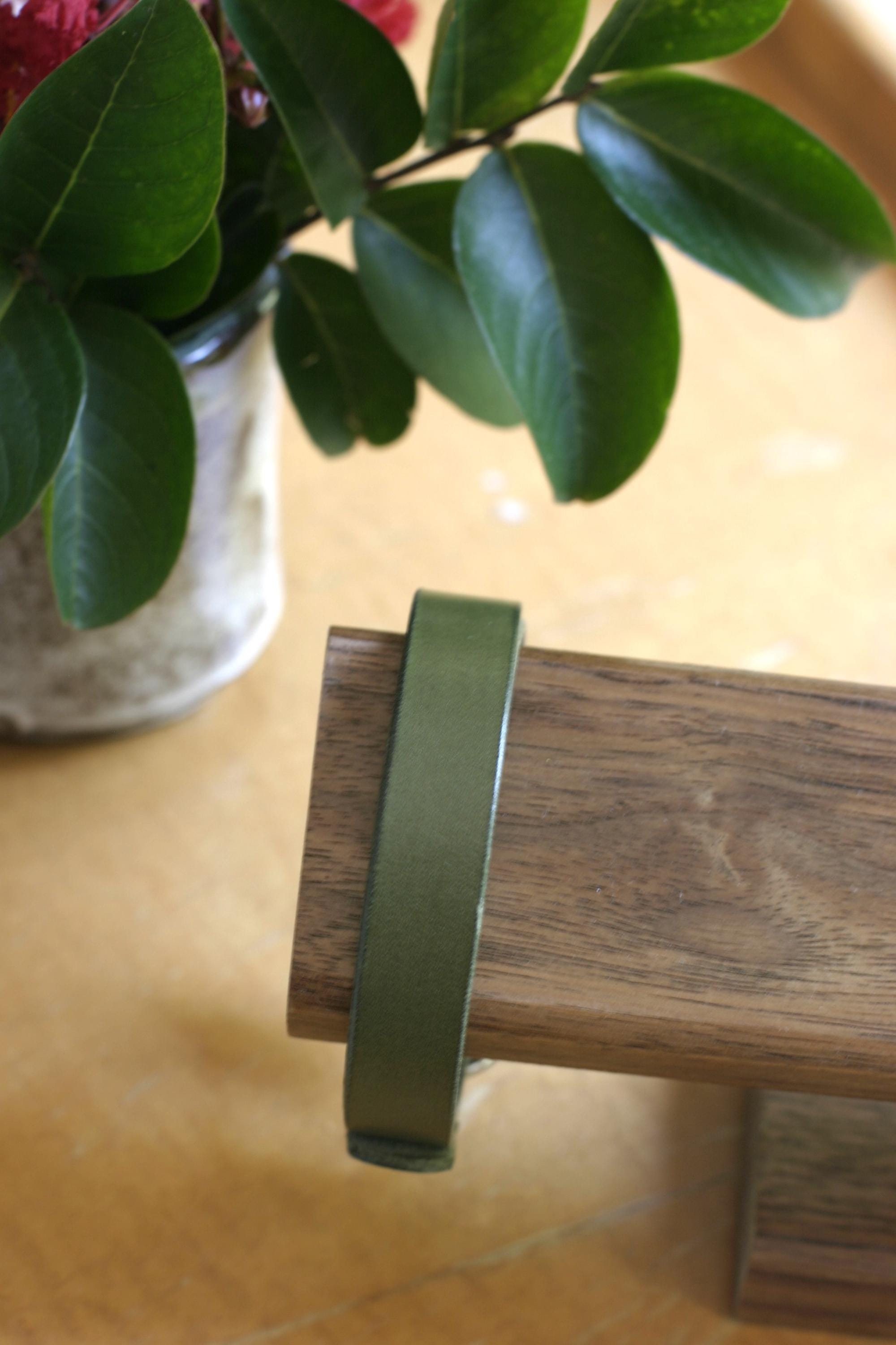 Green bracelet on a wooden surface with a blurred plant in the background