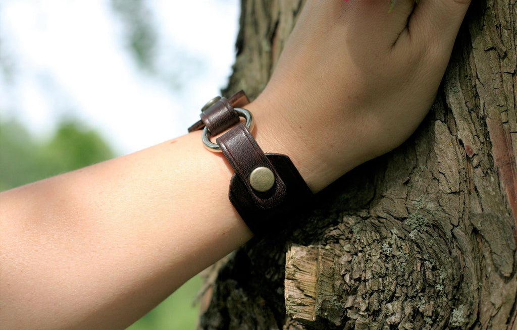 Brown leather bracelet on a wrist against a tree trunk background
