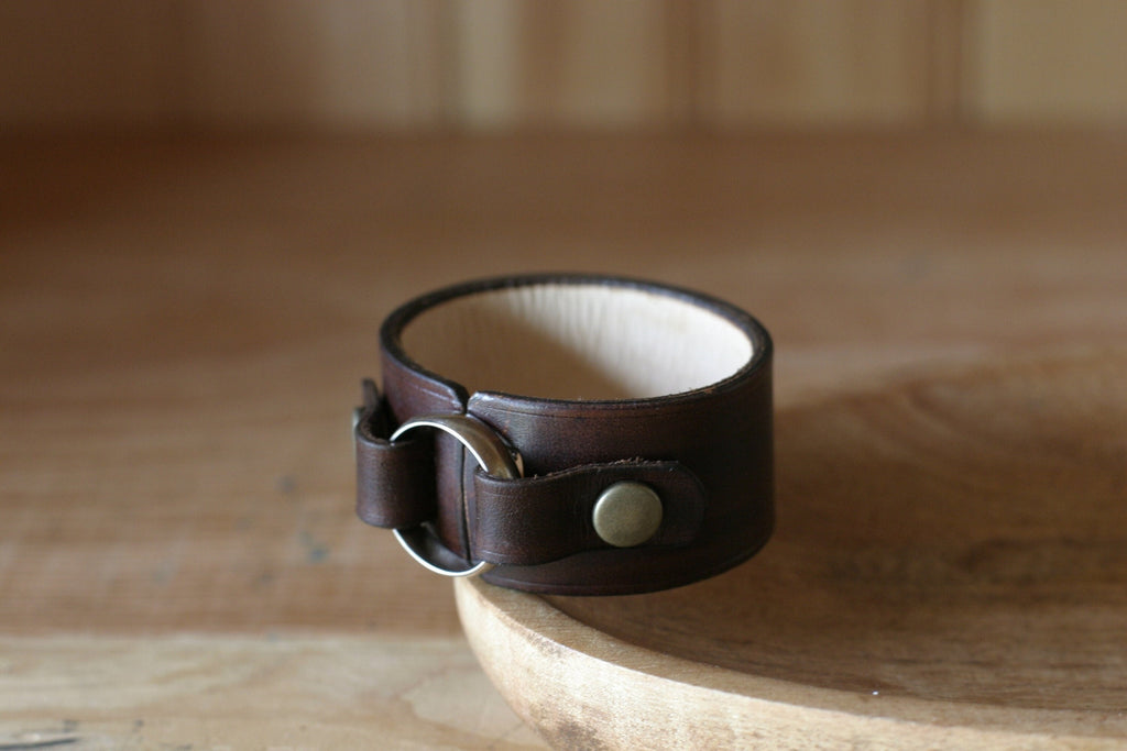 Brown leather bracelet with a metal clasp on a wooden surface