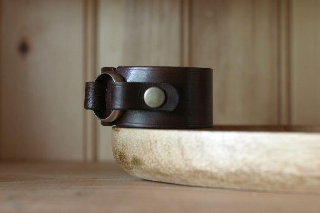 Brown leather bracelet with a silver button on a wooden surface