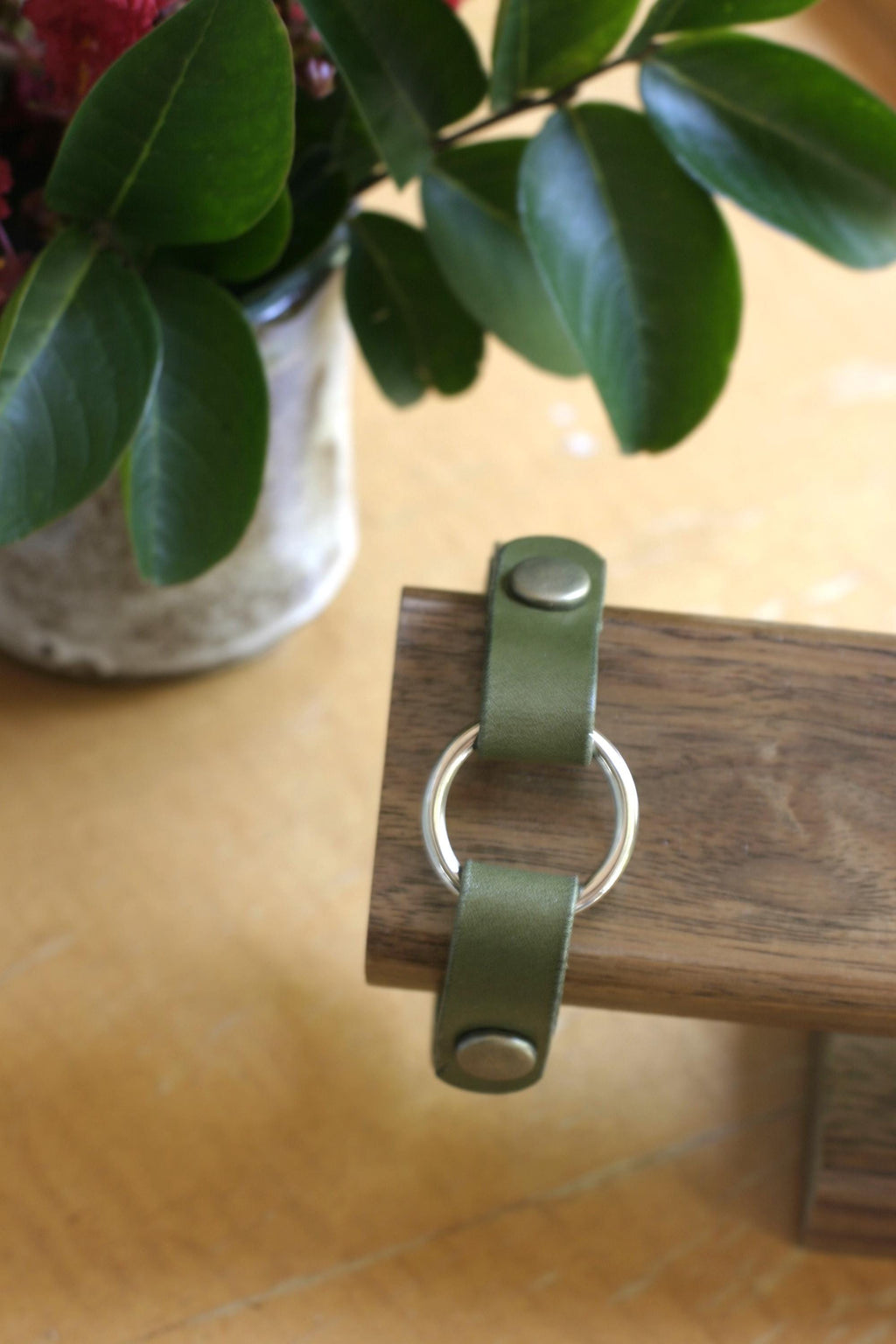 Green leather keychain with metal ring on a wooden surface next to a plant