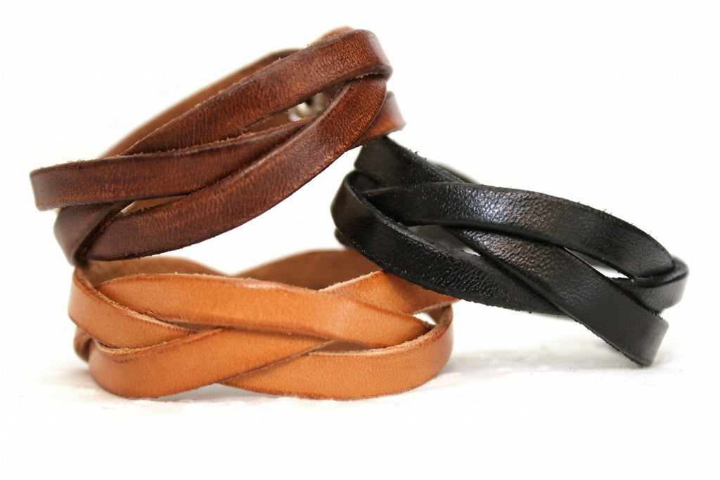 Three braided leather bracelets in brown, black, and orange on a light background