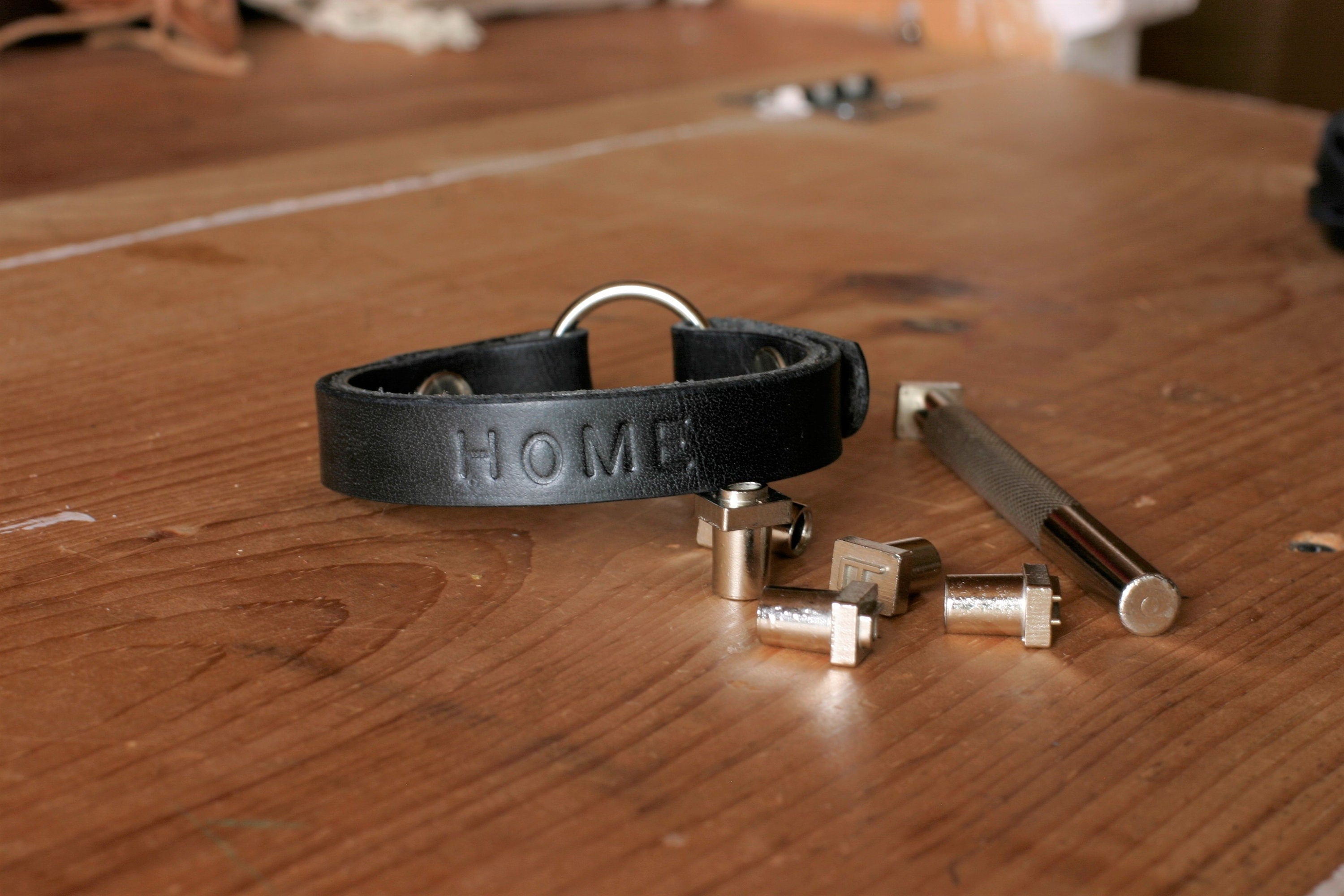 Black leather bracelet with 'HOME' engraving on a wooden surface