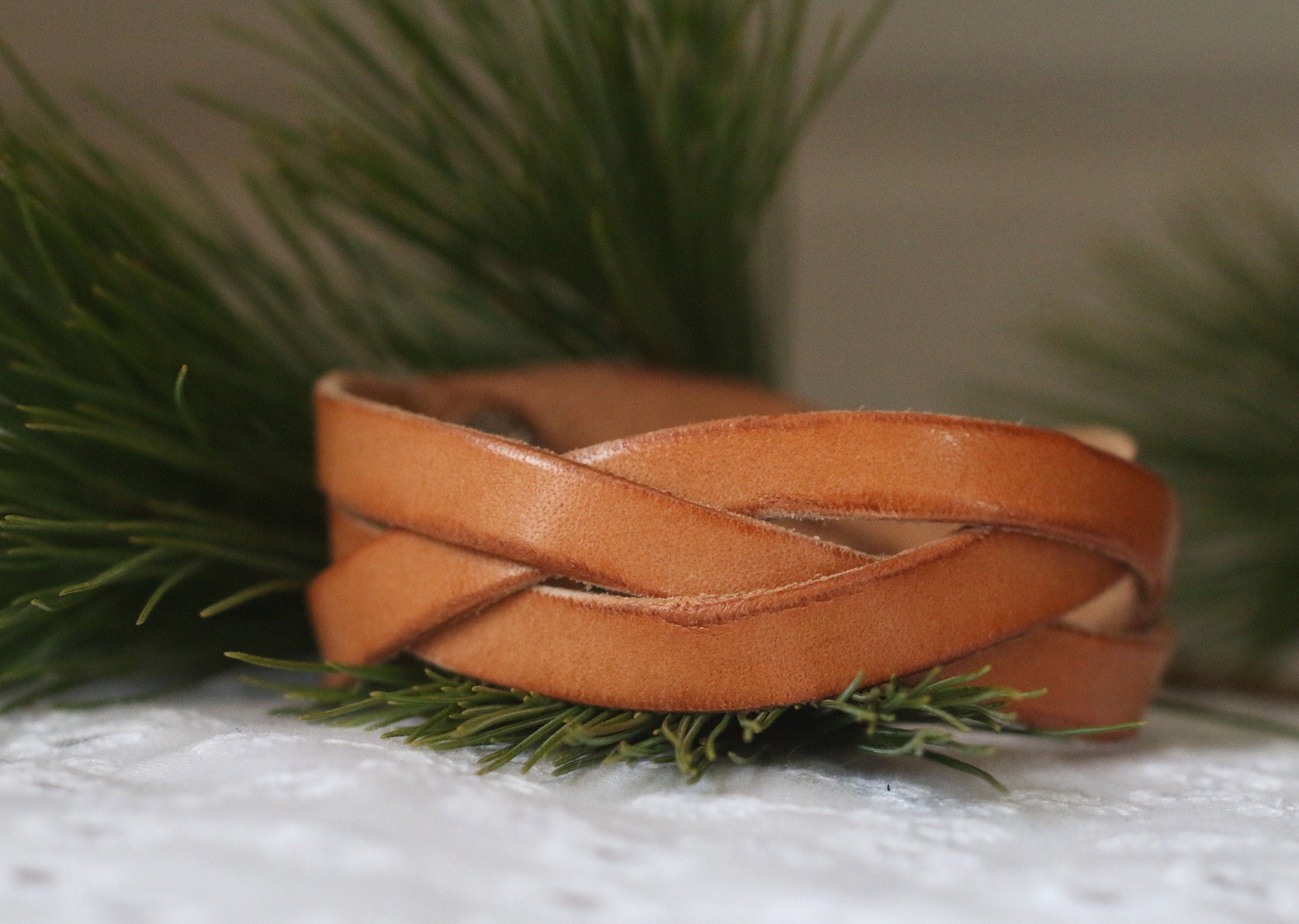 Brown leather bracelet on a white surface with greenery
