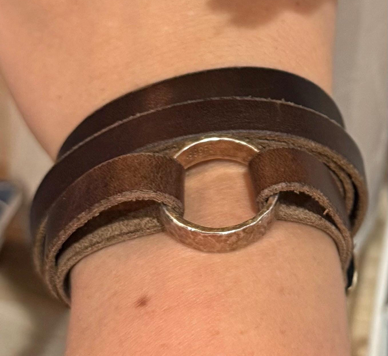 Hand wearing a brown leather bracelet with a blurred background