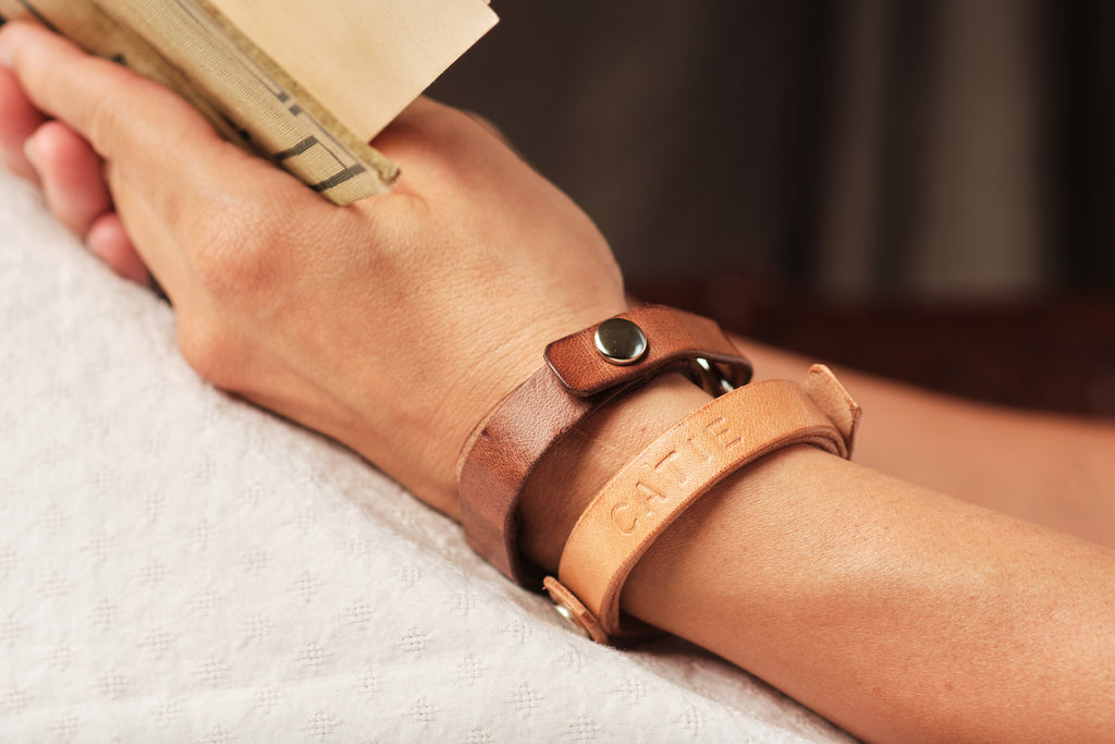 Close-up of a hand wearing a brown leather bracelet with a blurred background