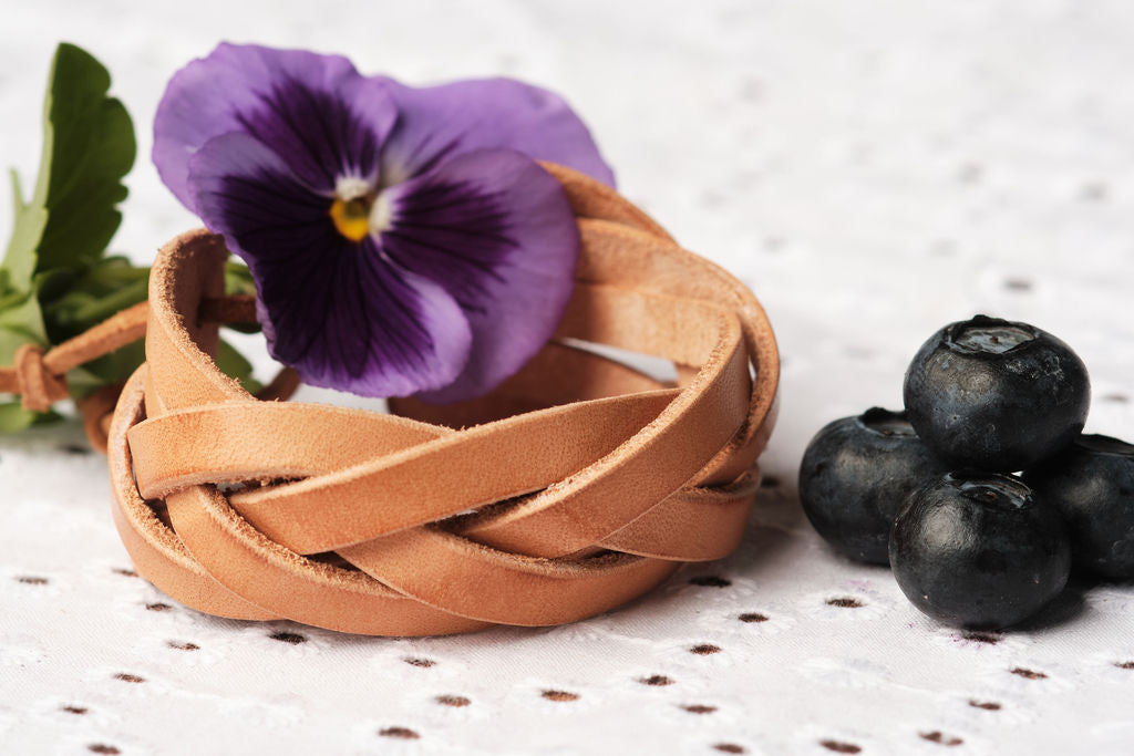 Brown woven bracelet with a purple flower and blueberries on a textured surface