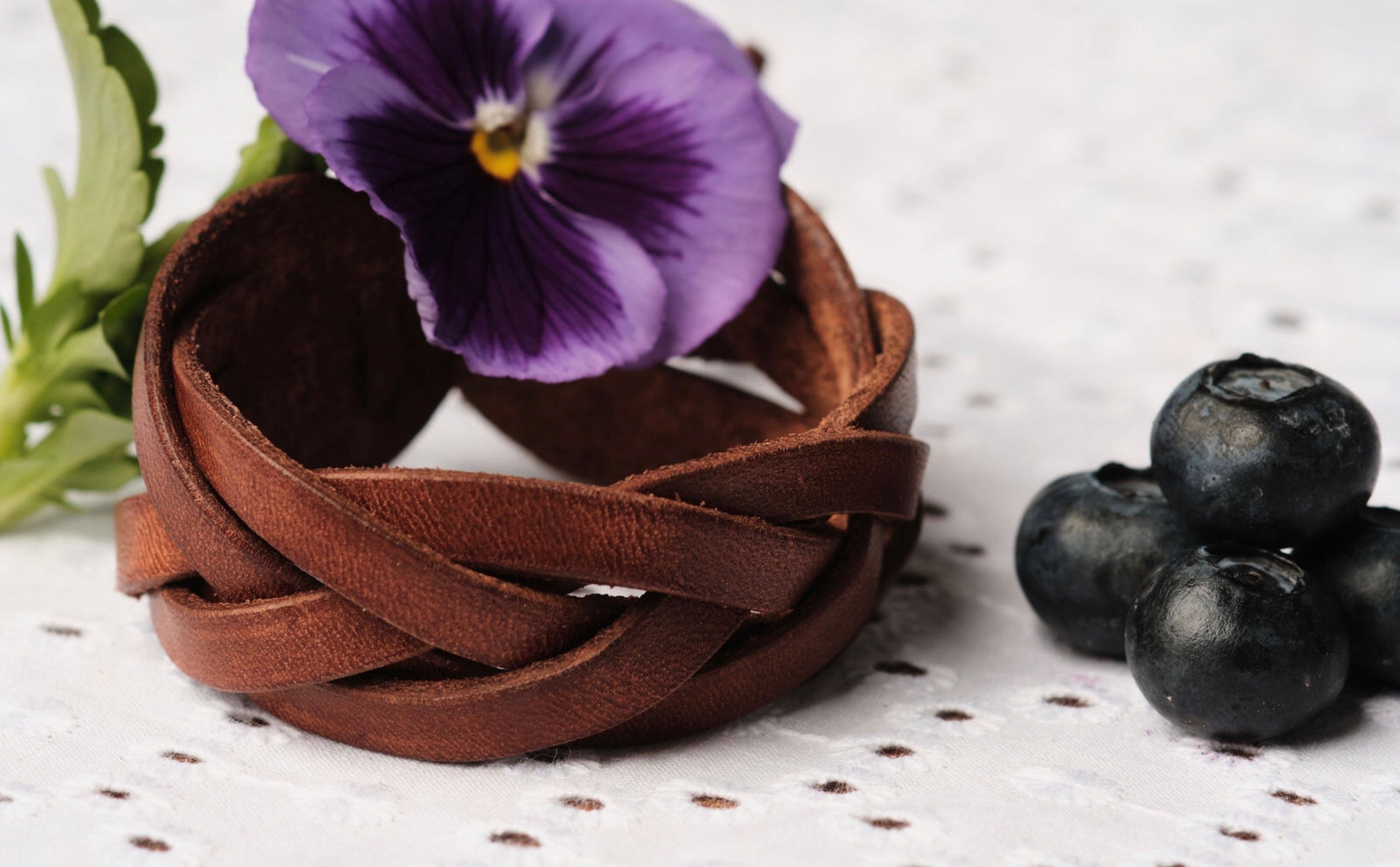 Brown woven bracelet with a purple flower and blueberries on a light background