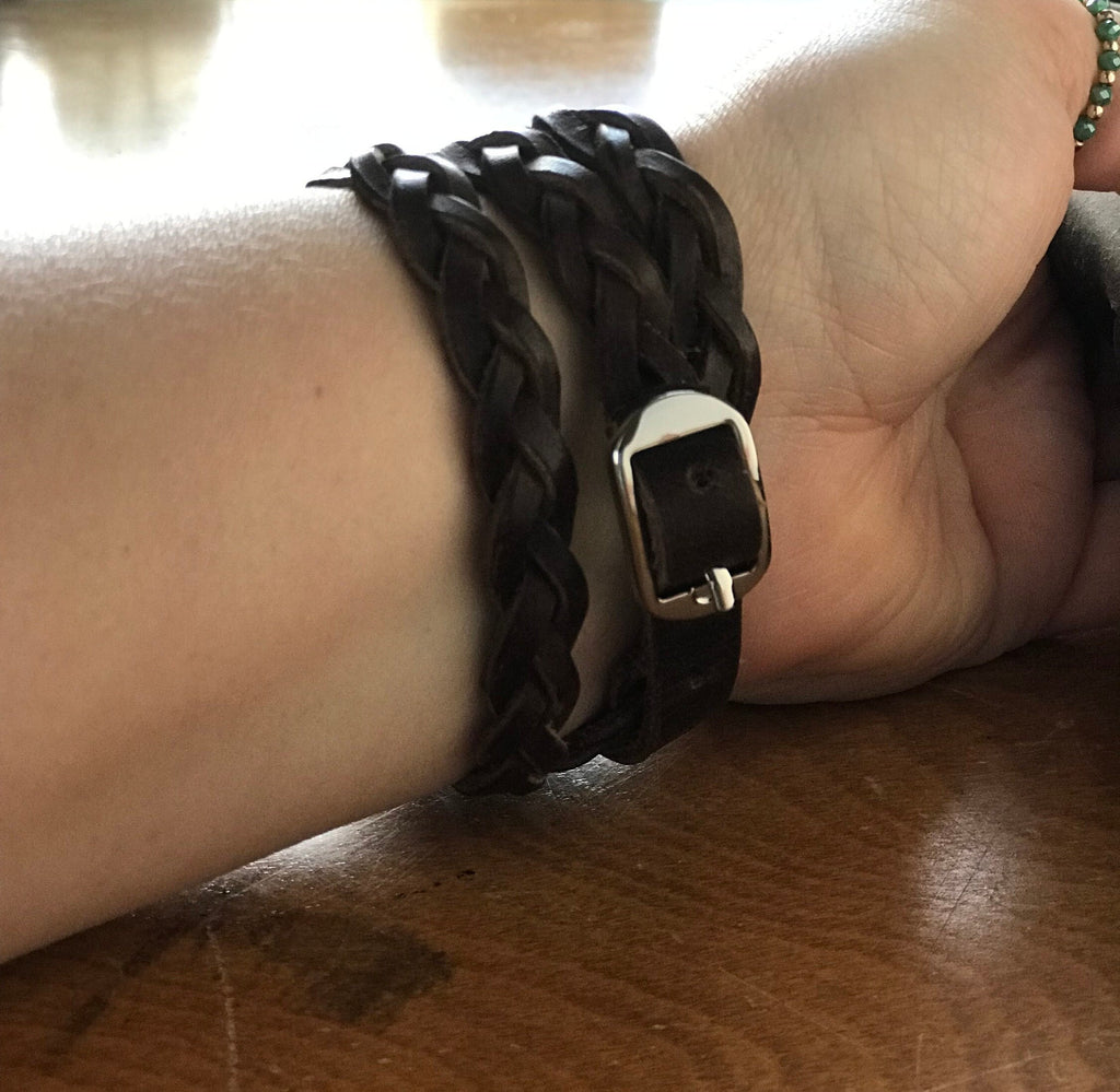 Close-up of a wrist wearing a black braided bracelet with a gold clasp on a wooden surface.
