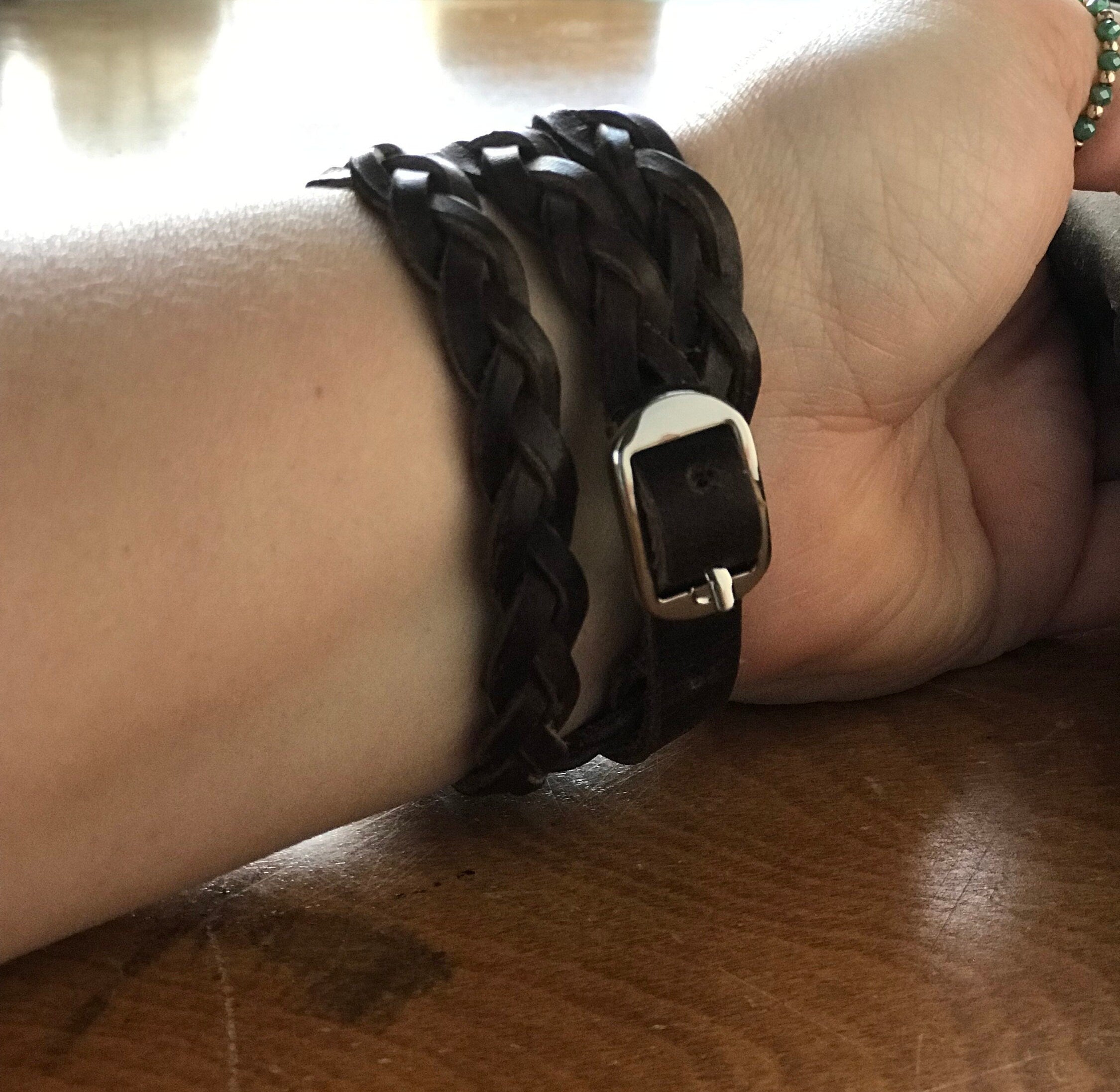Close-up of a wrist wearing a black braided bracelet with a gold clasp on a wooden surface.