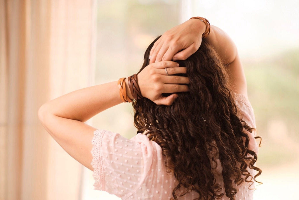 Woman with curly hair touching her head, wearing a pink top with a blurred background
