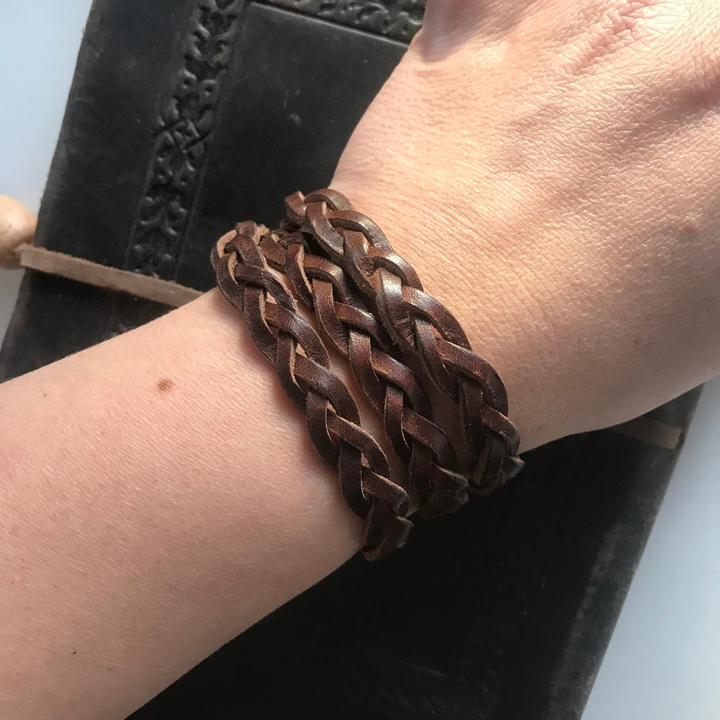 Brown braided leather bracelet on a wrist with a blurred background