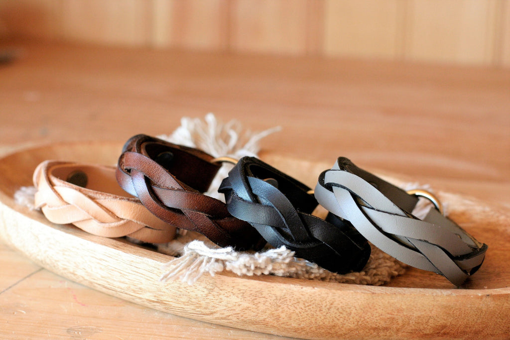 Three braided leather bracelets on a wooden tray with a blurred background