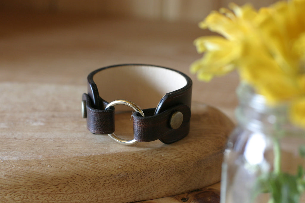 Black leather wear the ring with silver ring on a wooden surface with yellow flowers in the background