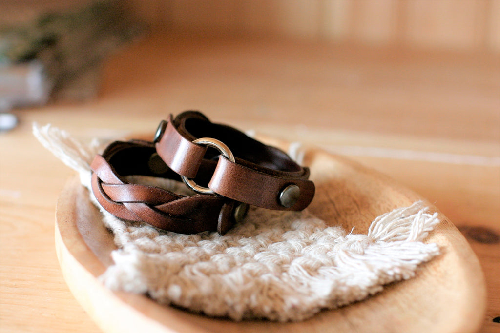 Two braided leather bracelets on a wooden surface with a blurred background