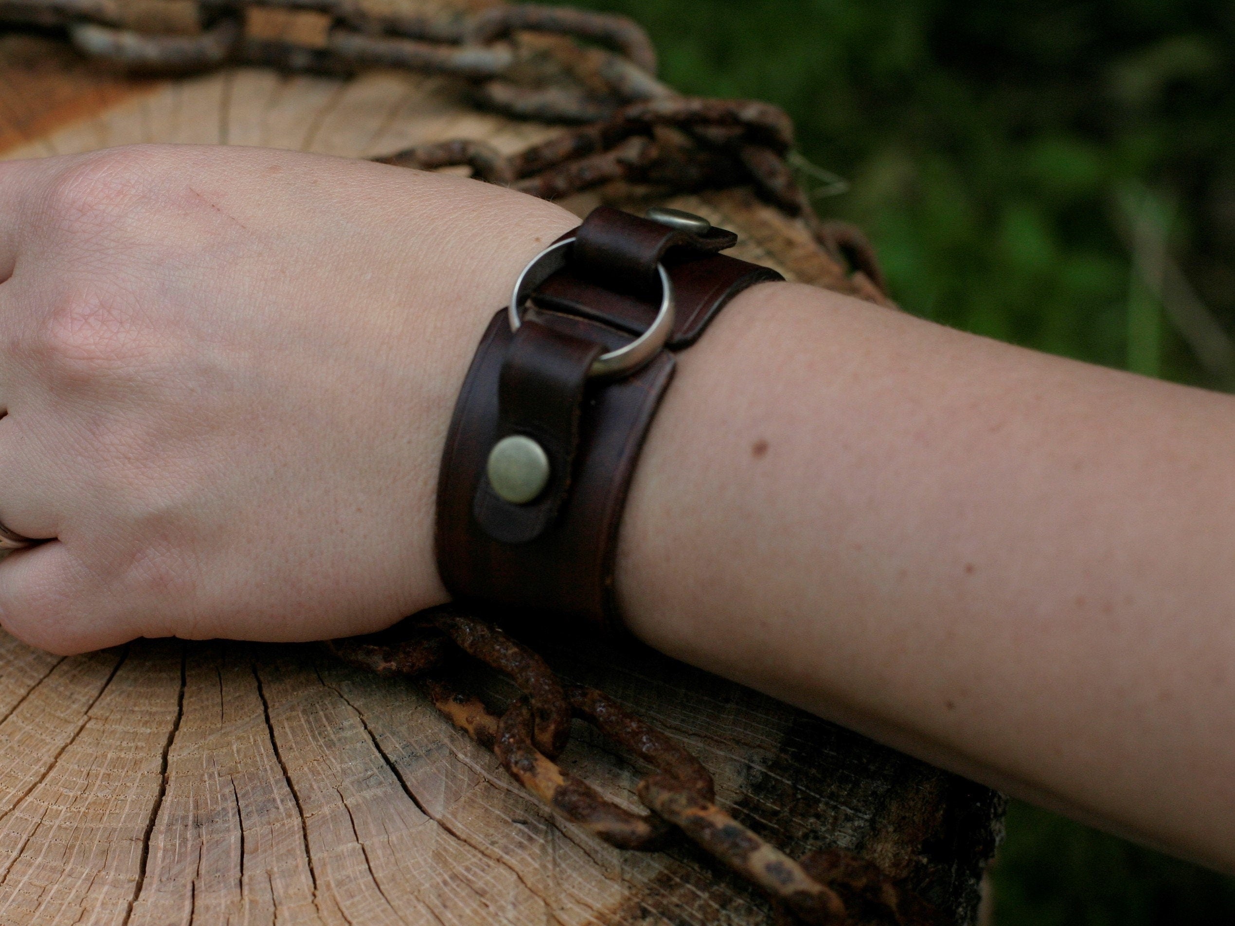 Brown leather bracelet with a metal clasp on a wrist, against a natural background.