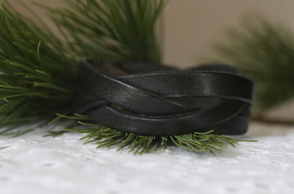 Black braided leather bracelet on a white surface with greenery in the background