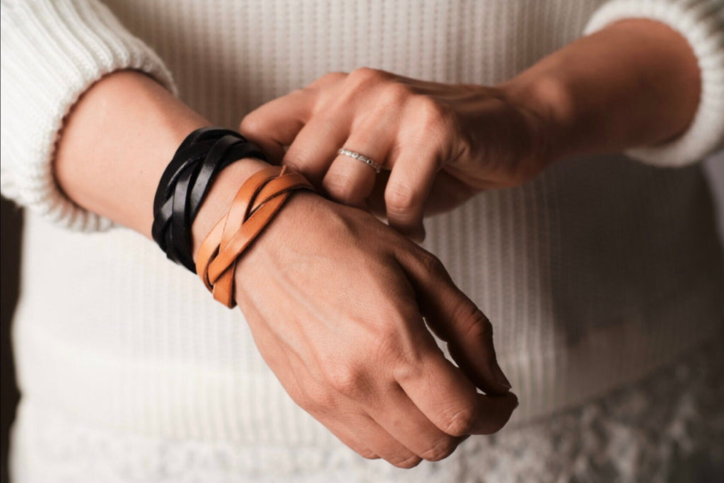 Close-up of hands wearing leather bracelets and a ring, with a blurred background.