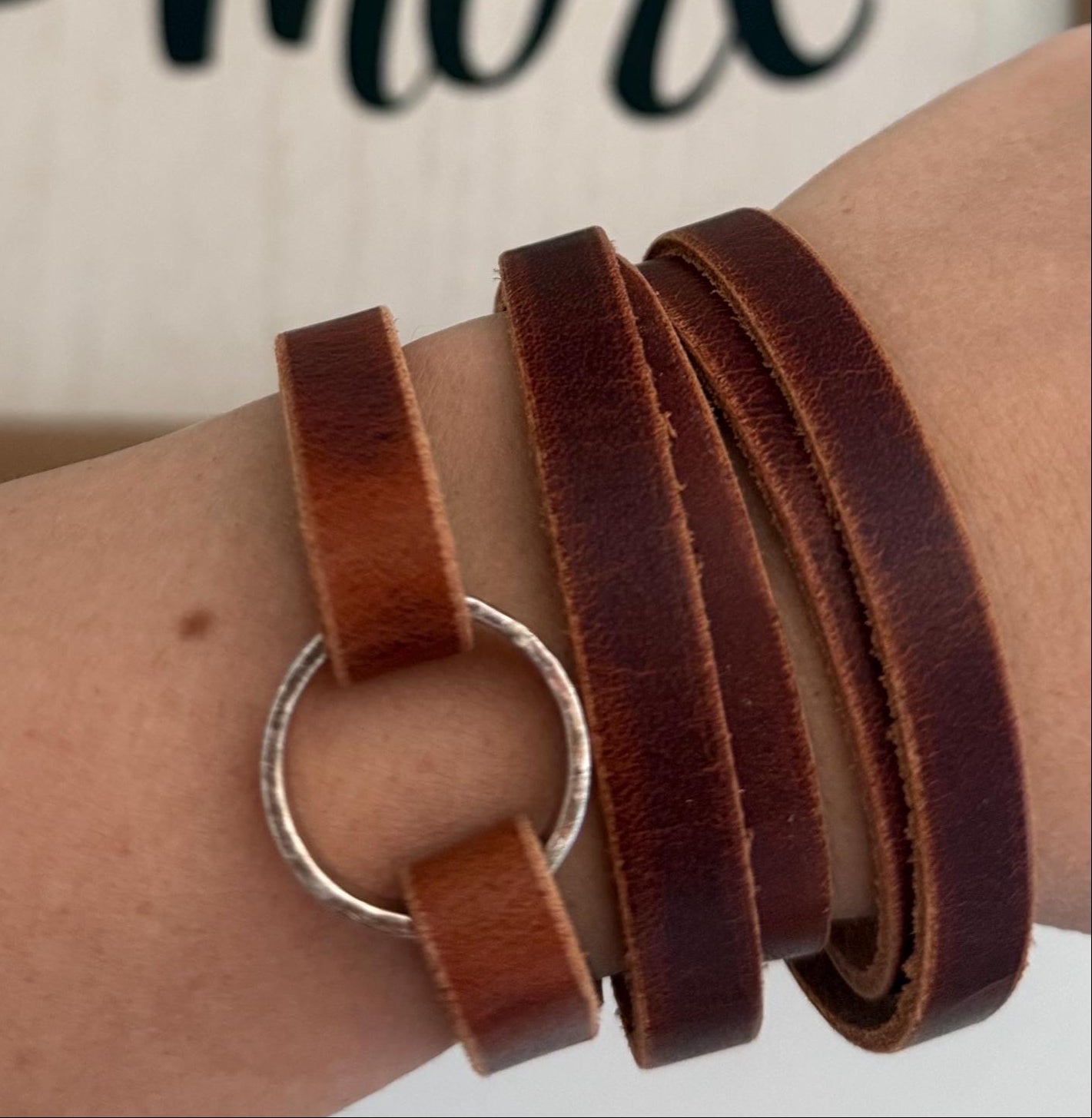 Brown leather wrap bracelet on wrist with 'I love you more' text in the background