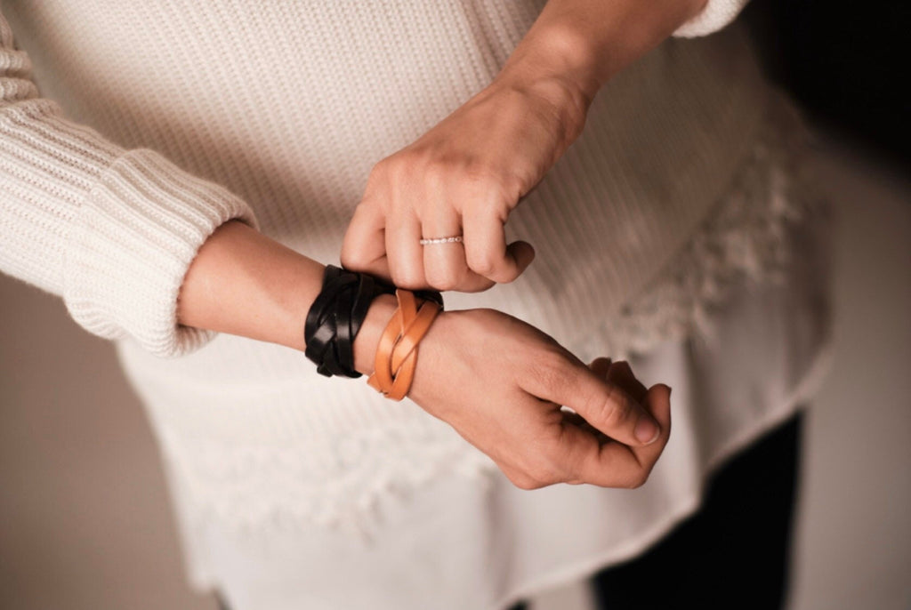 Person adjusting leather bracelets on their wrist against a neutral background